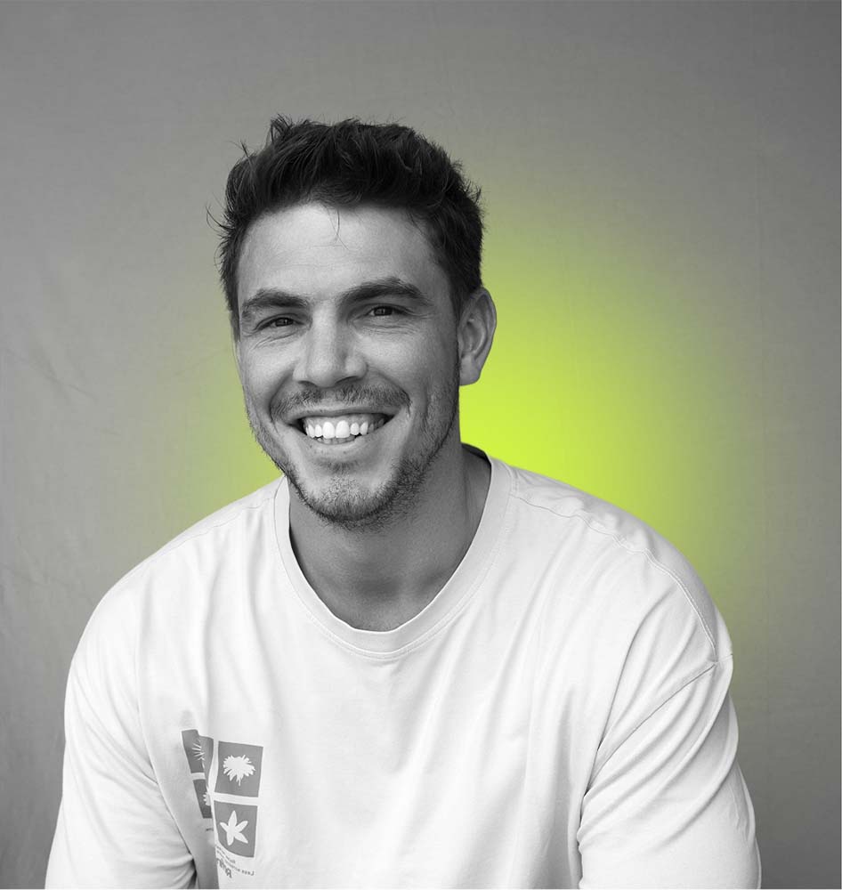 Smiling man in a white shirt against a gray background with a yellow-green glow. The tone is cheerful and relaxed.