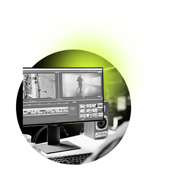 A grayscale image of a person editing video on a computer screen, highlighted by a green glow. The workspace is modern, conveying focus and creativity.