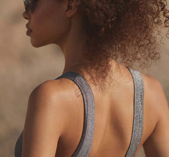 Woman with curly hair and sunglasses in profile, wearing a metallic gray top. The lighting is warm, creating a serene and confident mood.